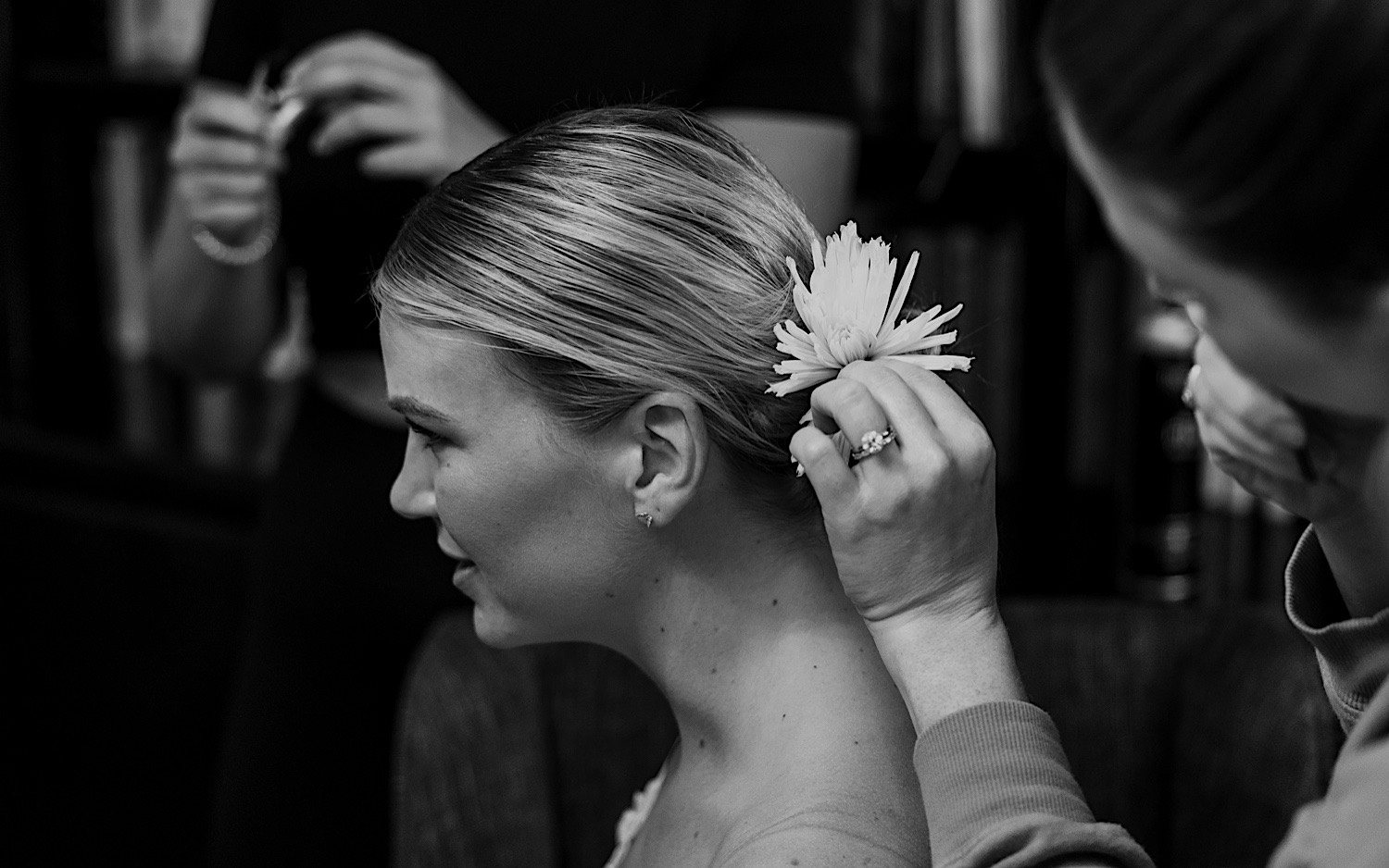Black and white photo of a bride having a flower put into her hair as she gets ready for her wedding