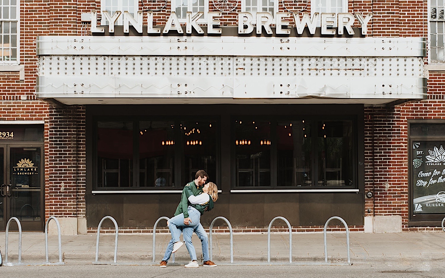 A man dips a woman as the two stand in front of a closed theater during their engagement photos in the Twin Cities A man dips a woman as the two stand in front of a closed theater during their engagement photos in the Twin Cities