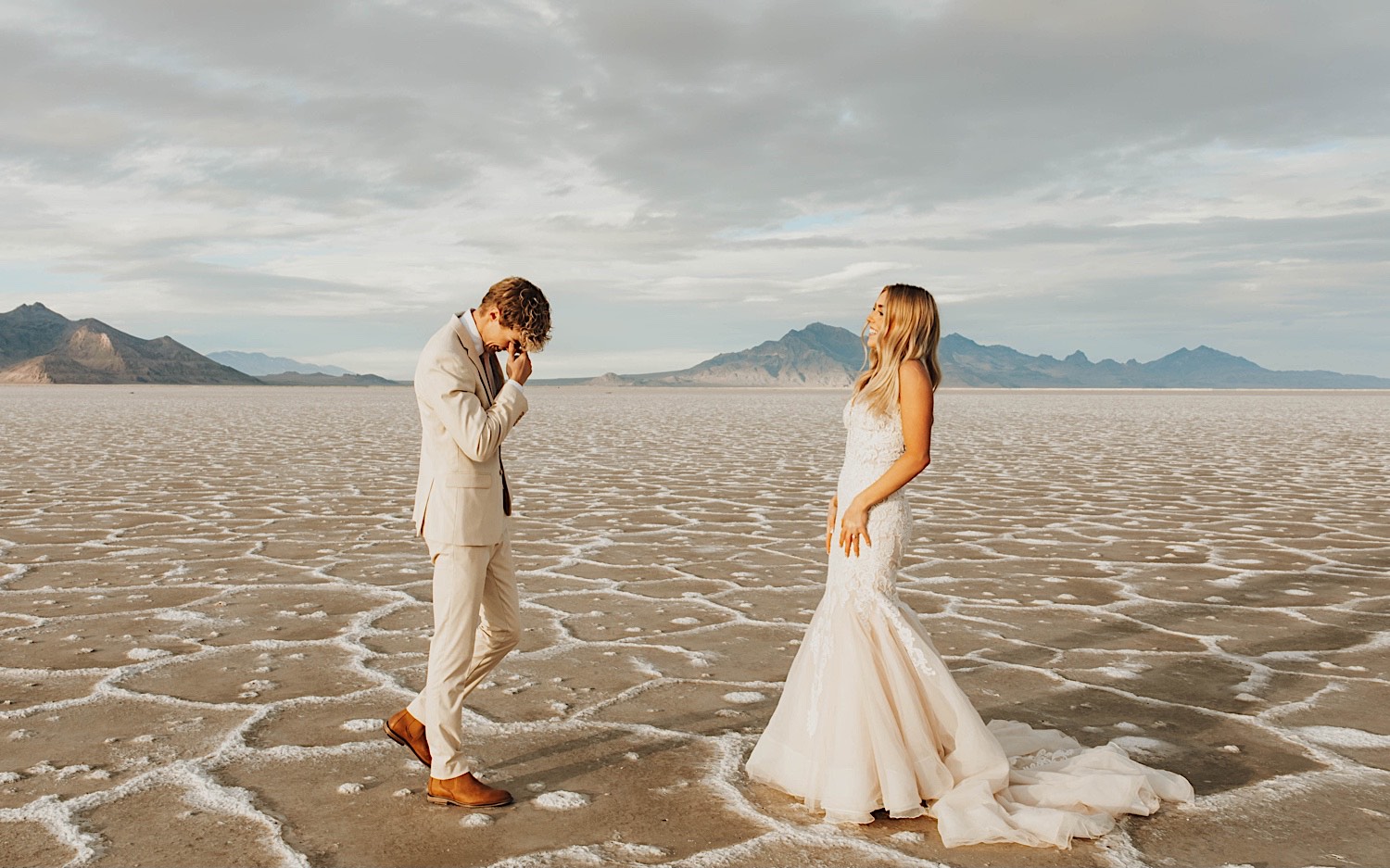 In the Utah Salt Flats, a groom gets emotional seeing the bride for the first time as she smiles at him before their elopement ceremony In the Utah Salt Flats, a groom gets emotional seeing the bride for the first time as she smiles at him before their elopement ceremony