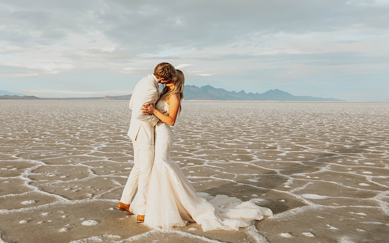 At their elopement in the Utah Salt Flats a bride and groom in their wedding attire kiss one another At their elopement in the Utah Salt Flats a bride and groom in their wedding attire kiss one another