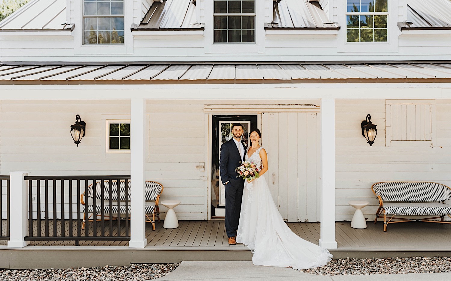 A bride and groom stand outside of a building of their wedding venue Legacy Hill Farms in Minnesota, they smile at the camera while holding one another
