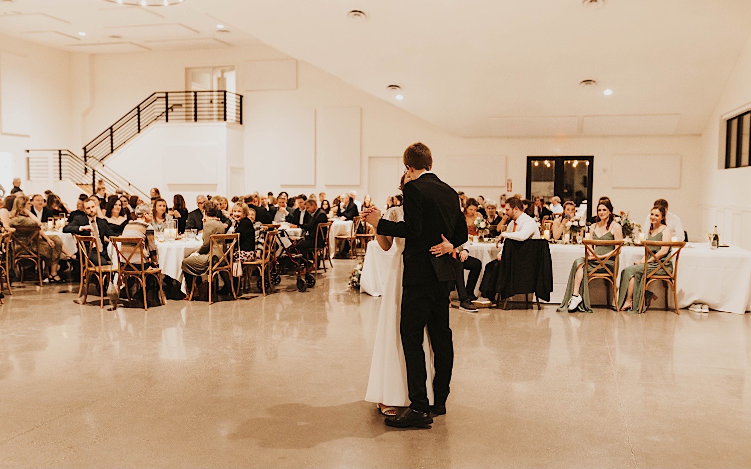 A bride and groom share their first dance together while guests watch during their indoor reception at Woodhaven Weddings + Events