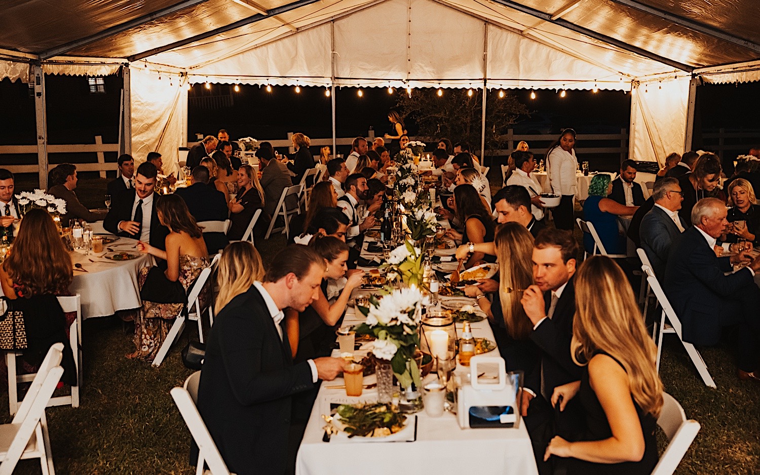 A wedding reception takes place underneath a large string lit tent