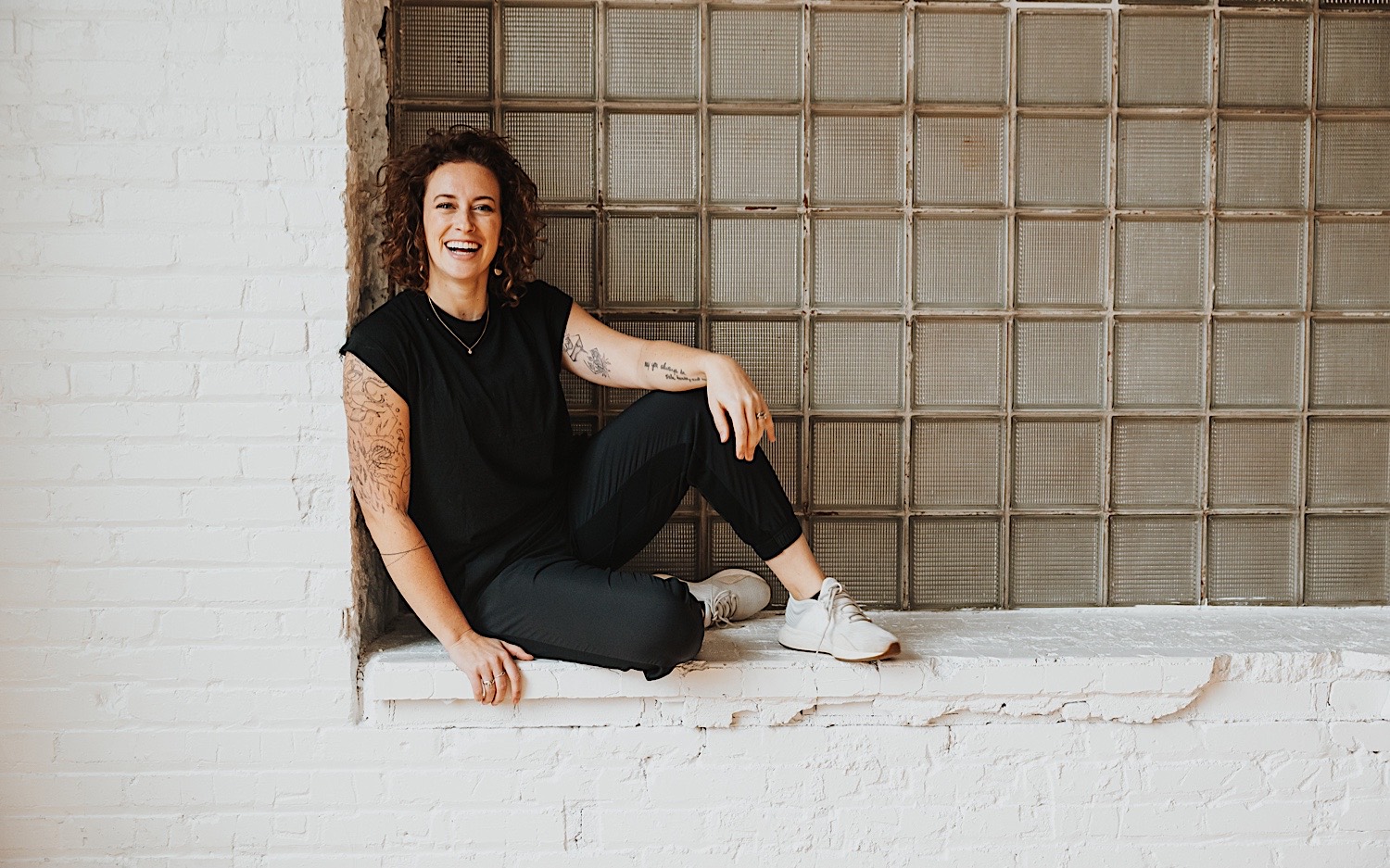 Chelsea, a wedding photographer in Minneapolis, and owner of Sage River Studios, sits on a windowsill and smiles at the camera