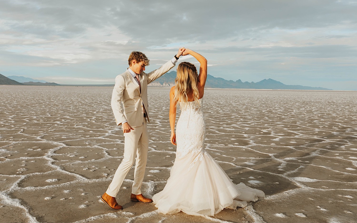 During their elopement in the Utah Salt Flats, a bride dances with the groom as he spins her around while holding her hand During their elopement in the Utah Salt Flats, a bride dances with the groom as he spins her around while holding her hand