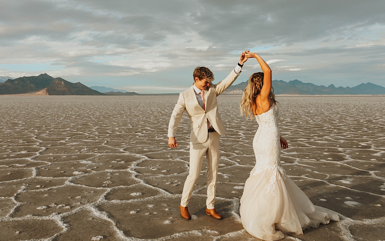 During their elopement in the Utah Salt Flats, a bride dances with the groom as he spins her around while holding her hand During their elopement in the Utah Salt Flats, a bride dances with the groom as he spins her around while holding her hand