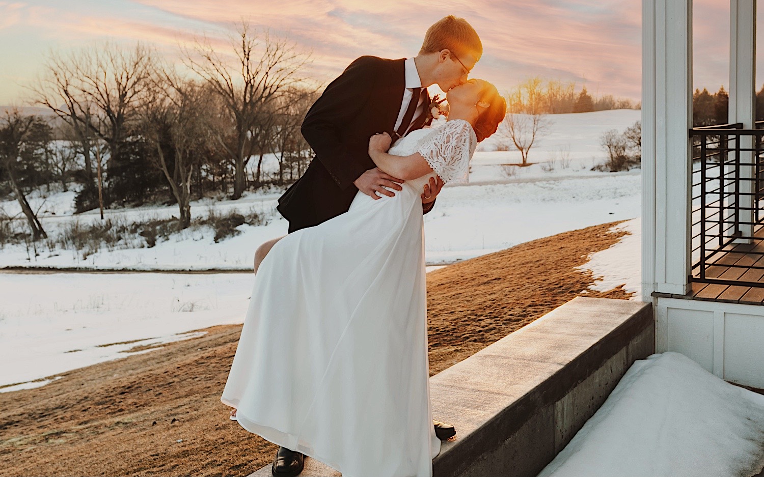 A bride and groom kiss under the sunset while on the back patio of their wedding venue, Woodhaven Weddings + Events