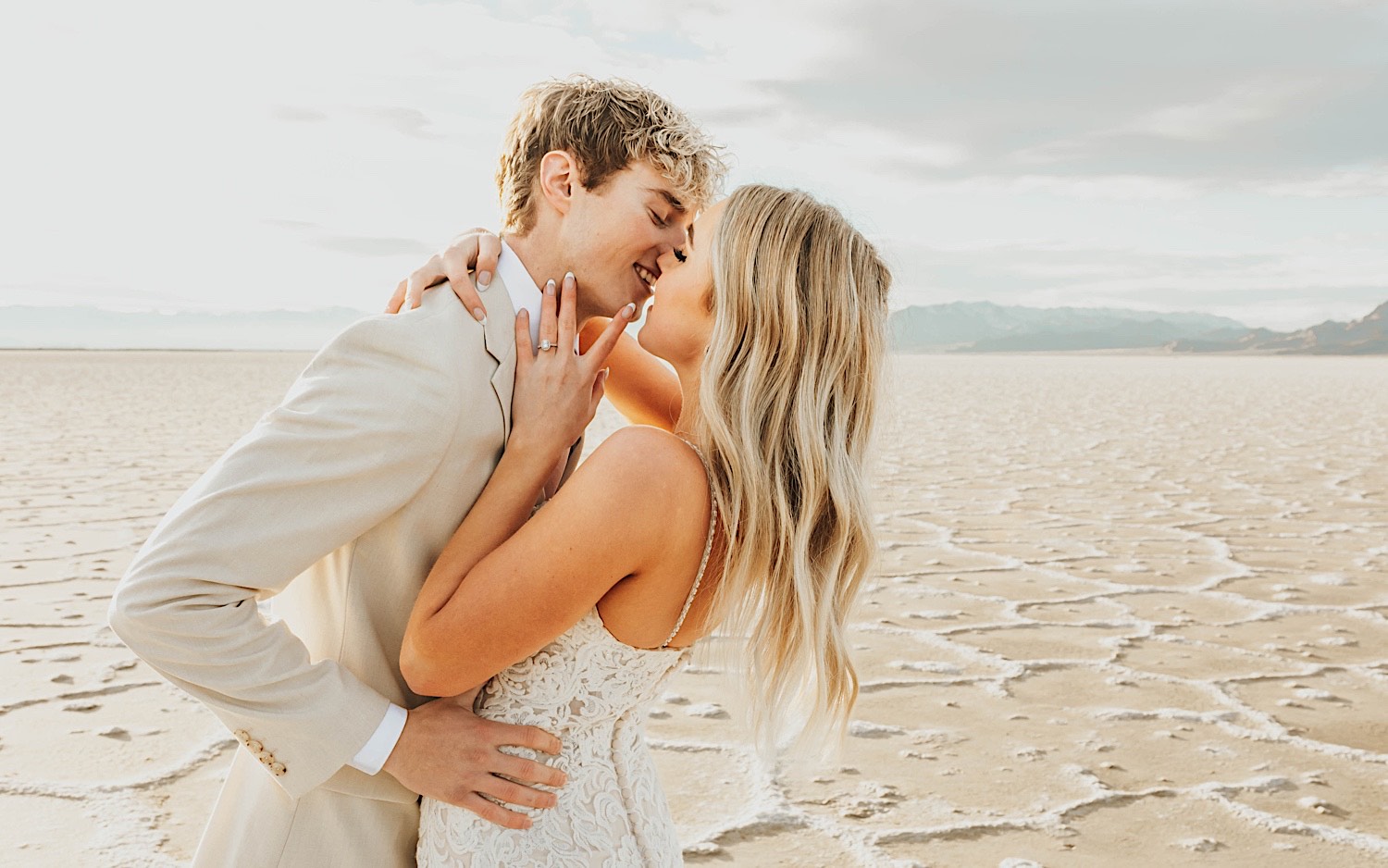A bride and groom embrace in the Utah Salt Flats on their elopement day, the groom is smiling as they are about to kiss A bride and groom embrace in the Utah Salt Flats on their elopement day, the groom is smiling as they are about to kiss
