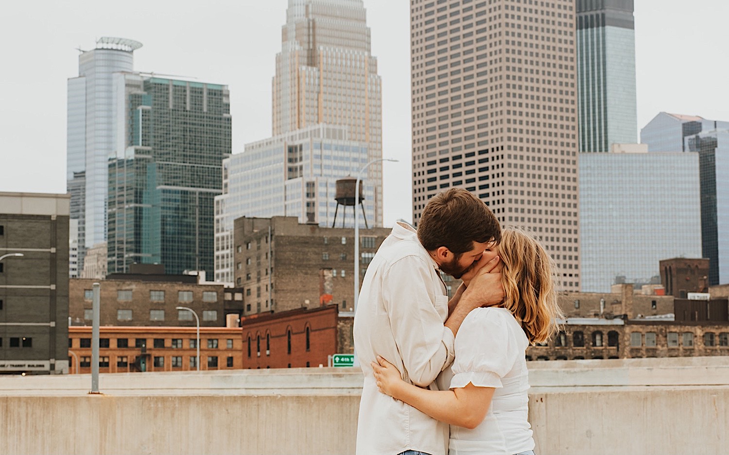 A couple kiss one another while having their engagement photos taken on the top level of a parking garage in downtown Minneapolis