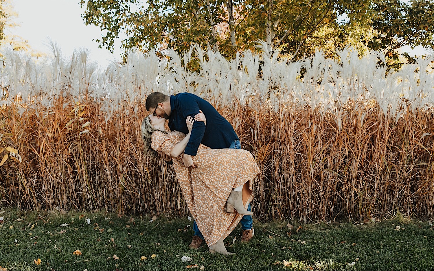 During a fall engagement session in Winona a woman is dipped and kissed by a man as they stand in front of a field During a fall engagement session in Winona a woman is dipped and kissed by a man as they stand in front of a field