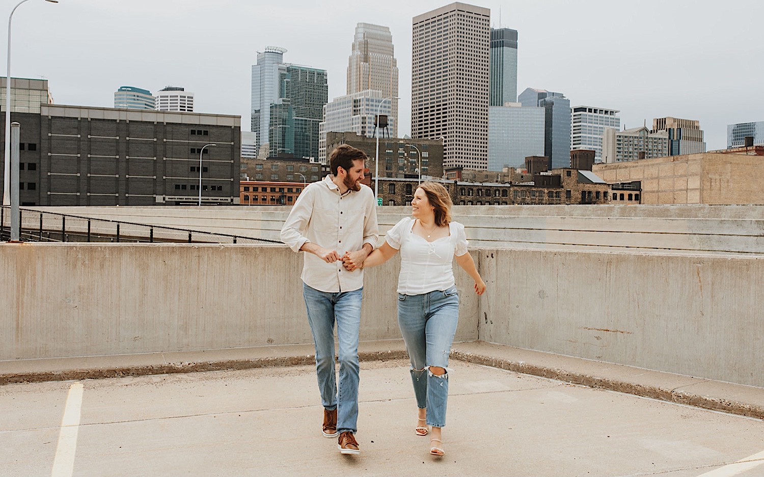 A couple smile at one another while running towards the camera while atop a parking garage in downtown Minneapolis