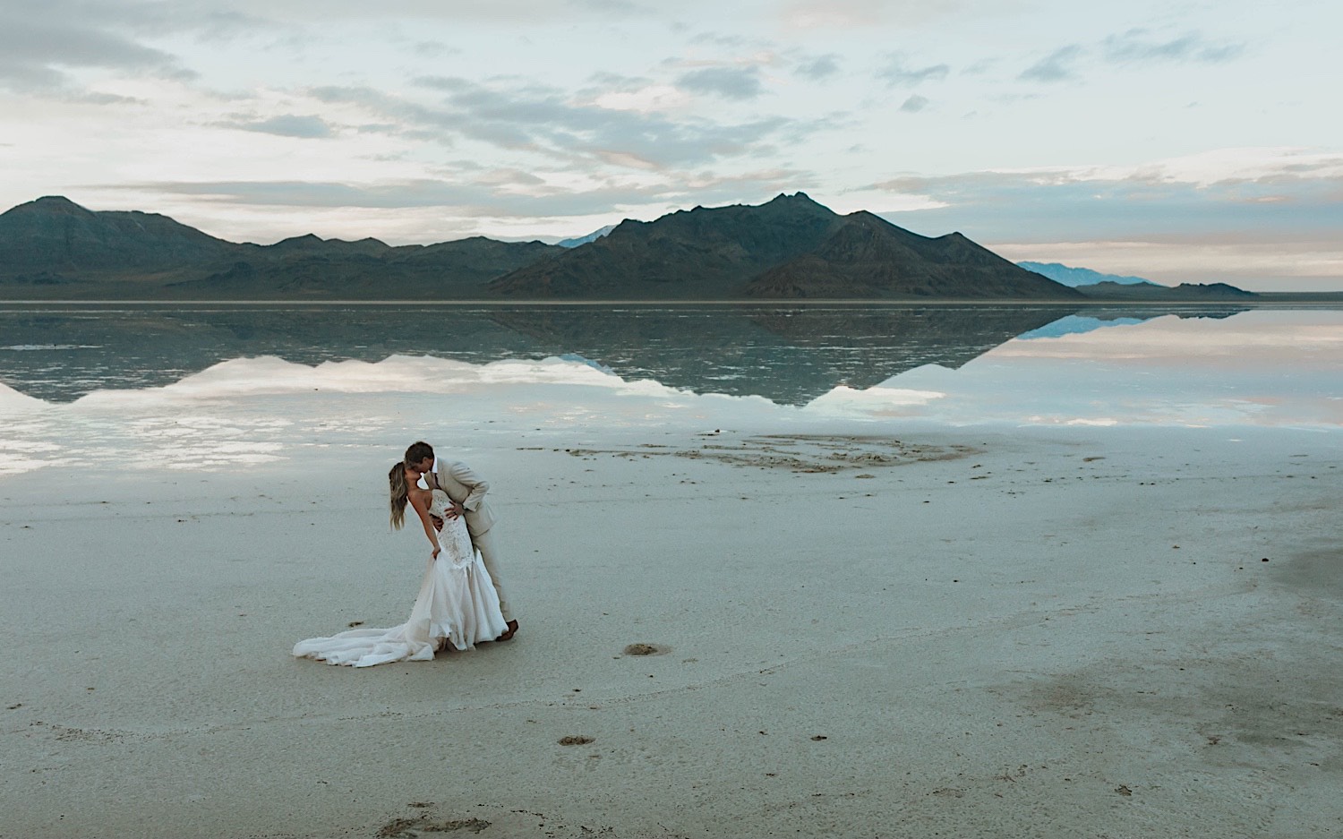 A bride is dipped and kissed by the groom while standing in the Utah Salt Flats during their elopement day A bride is dipped and kissed by the groom while standing in the Utah Salt Flats during their elopement day