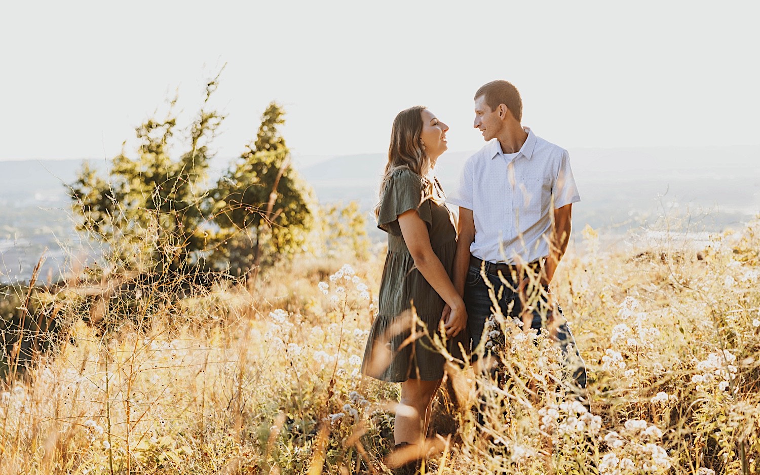 A couple smile at one another while holding hands atop a bluff in Minnesota during their engagement session in the fall