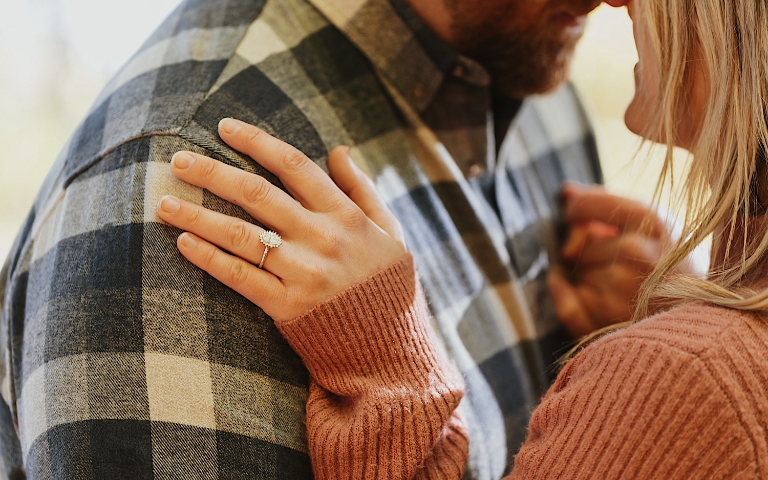 Close up photo of a woman's hand on a man's shoulder showing off the engagement ring on her finger