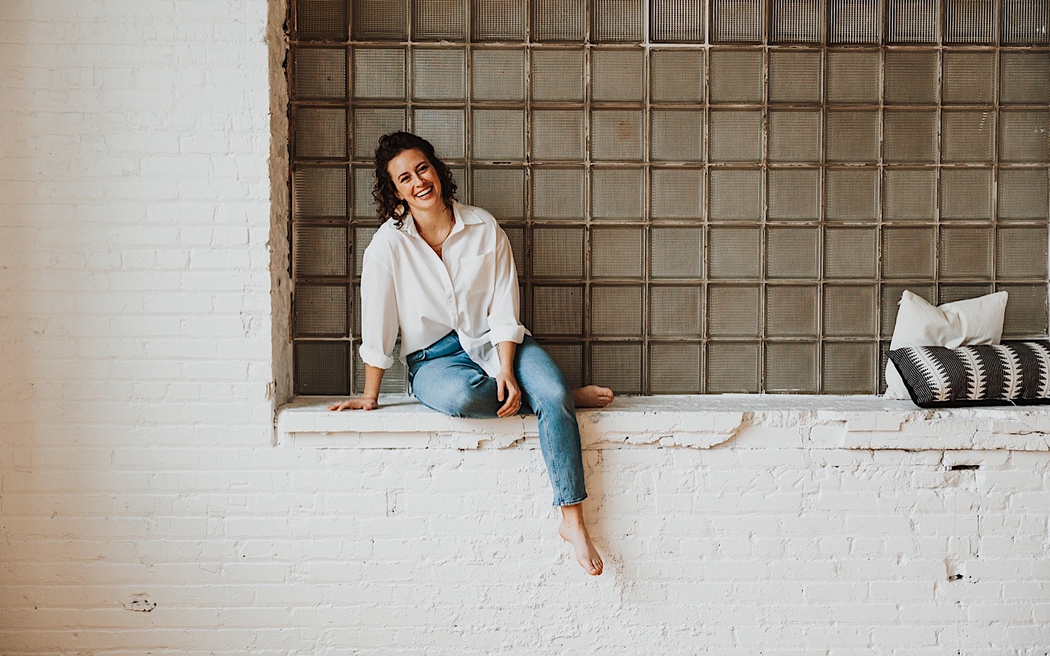 The Minnesota Wedding Photographer Chelsea of Sage River Studios sits on a brick windowsill and smiles at the camera