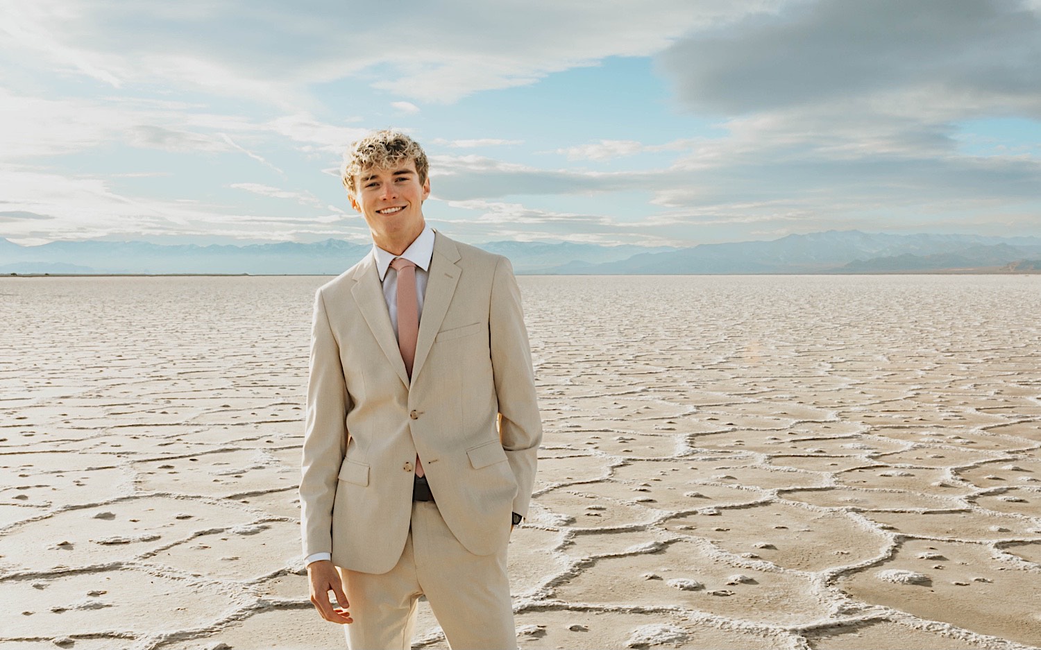 A groom standing in the Utah Salt Flats smiles at the camera before his elopement takes place