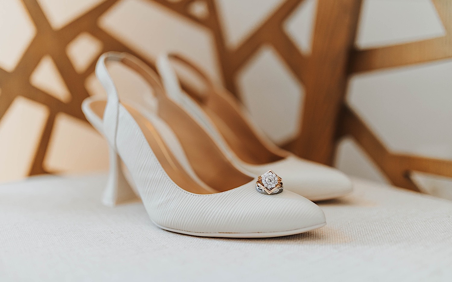 A wedding ring sits on a pair of white women's shoes which rest on a chair