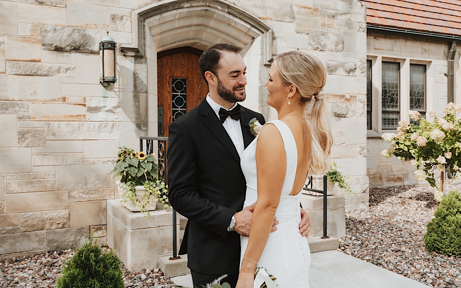 A bride and groom embrace and smile at one another outside a church