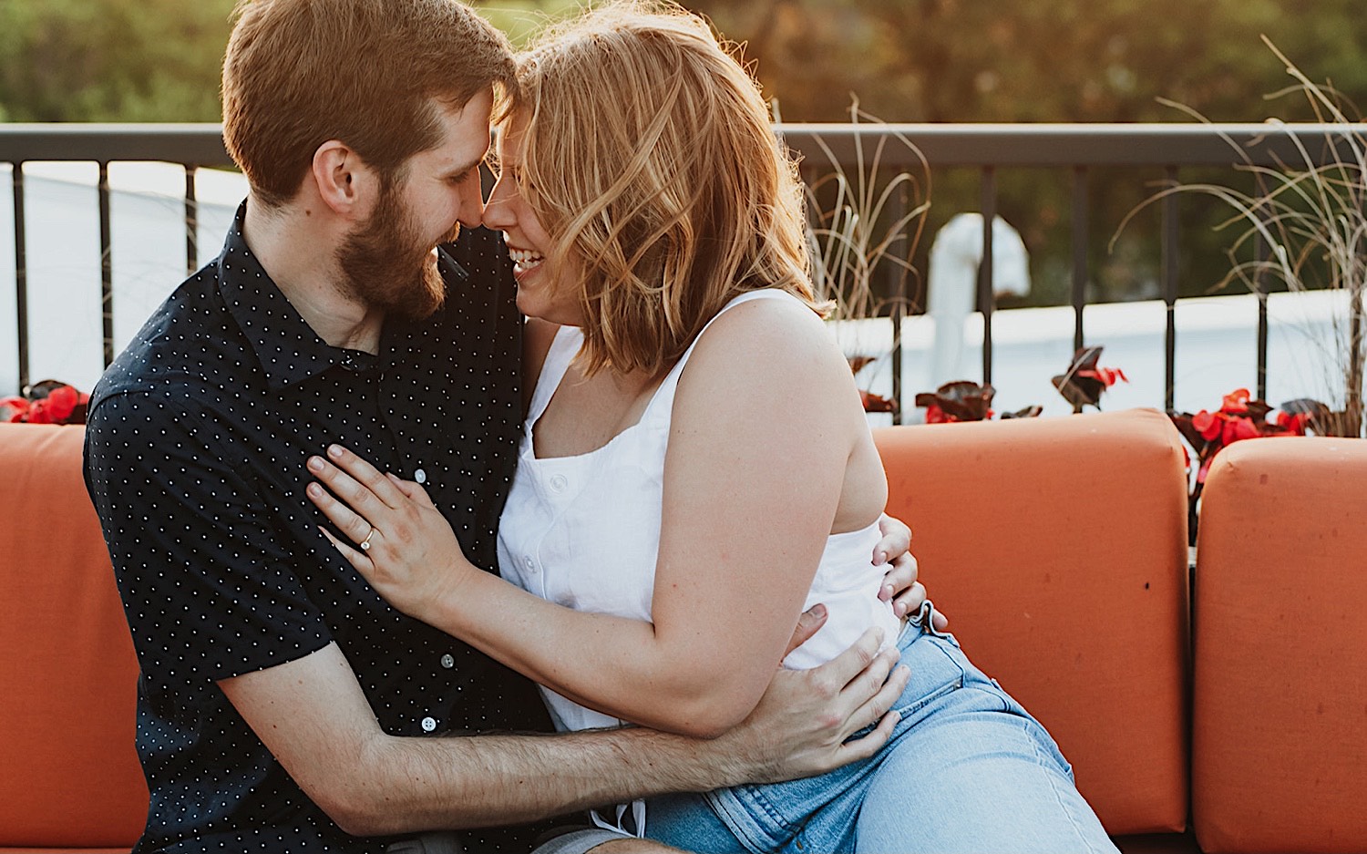 A couple smile at one another while sitting on a couch on the roof of their apartment in downtown Minneapolis during their engagement session