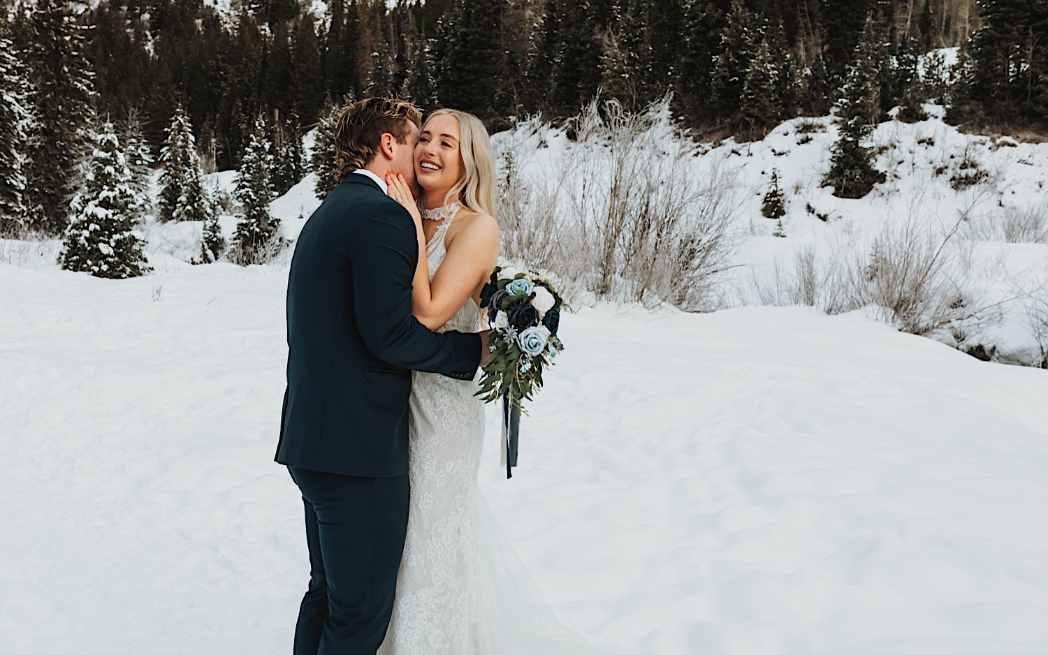 After their elopement, bride smiles as the groom kisses her on the cheek in a snow covered park near Salt Lake City