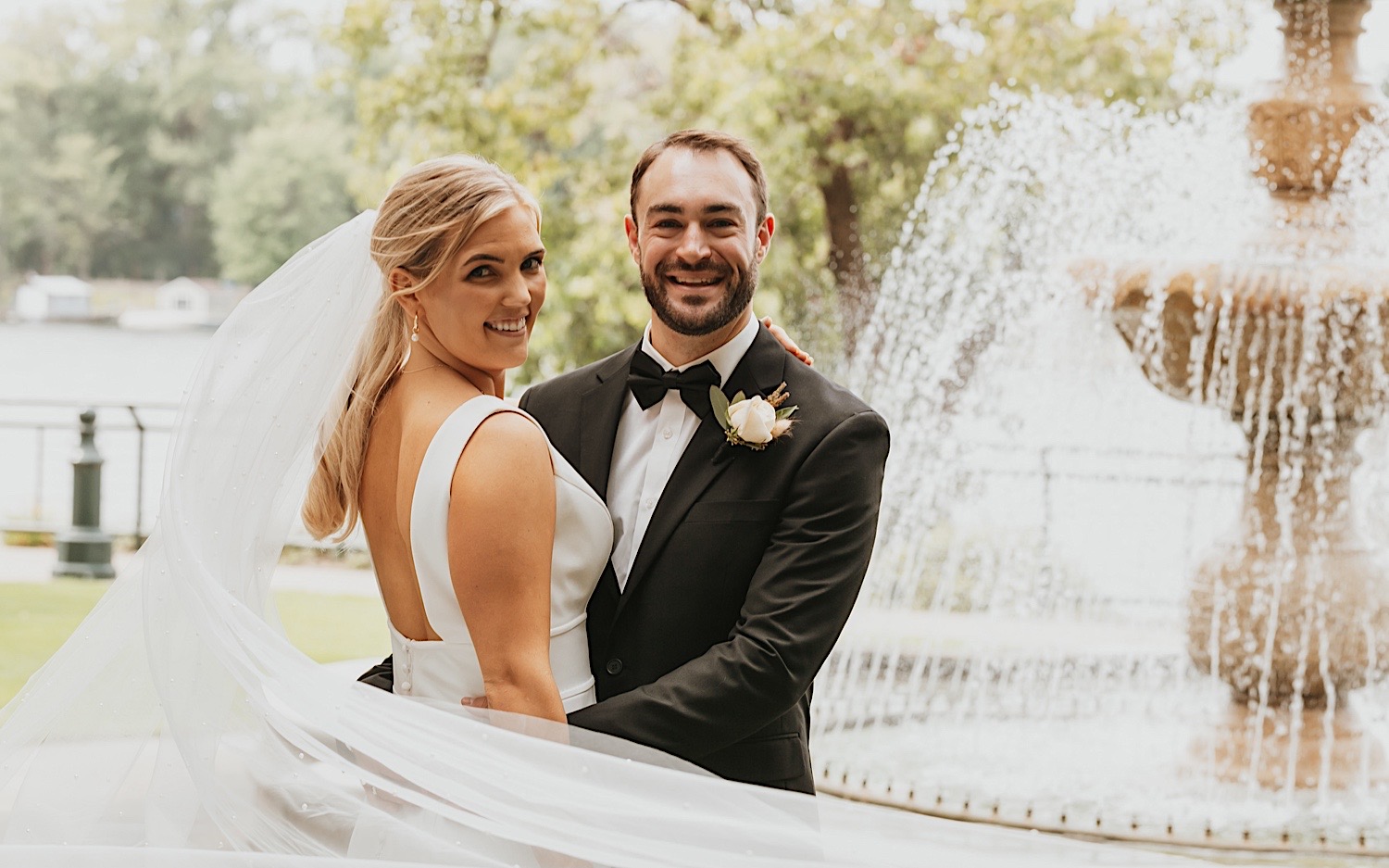 Portrait of a bride and groom smiling at the camera while embracing in front of a fountain