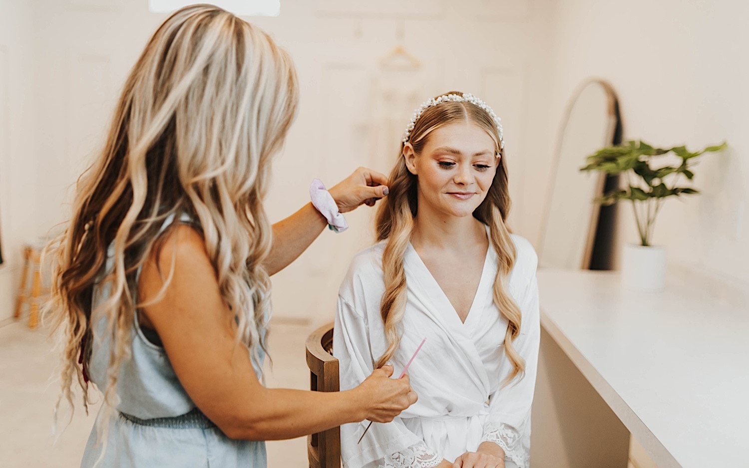 A bride sits in a chair as a woman works on her hair to get her ready for her wedding day at The Aisling A bride sits in a chair as a woman works on her hair to get her ready for her wedding day at The Aisling