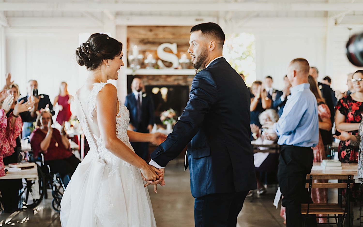 A bride and groom hold hands and share their first dance as guests watch during their indoor wedding reception at their venue Legacy Hill Farms in Minnesota