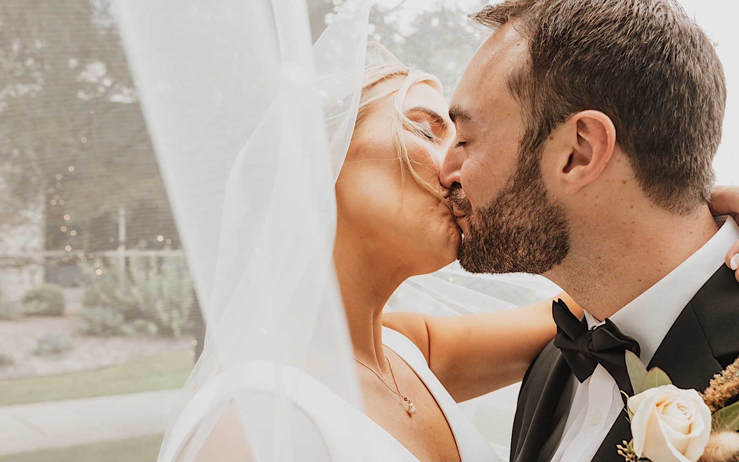 Close up photo of a bride and groom kissing one another as the bride's veil flows in the wind