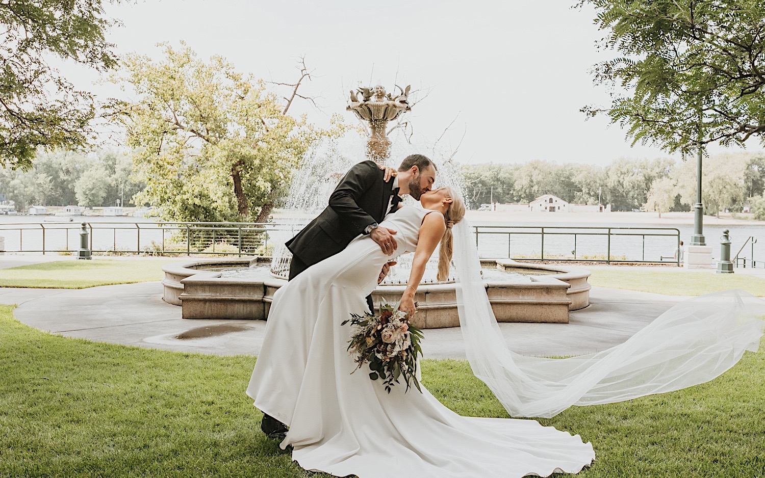 A groom dips his bride as they kiss in front of a fountain in La Crosse Wisconsin on their wedding day