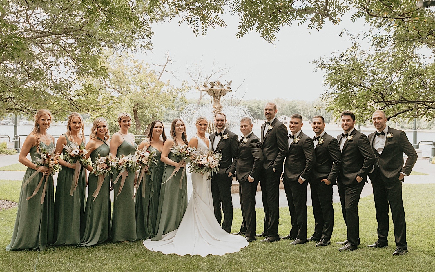 Portrait of a bride, groom, and their wedding parties smiling at the camera while in front of a fountain