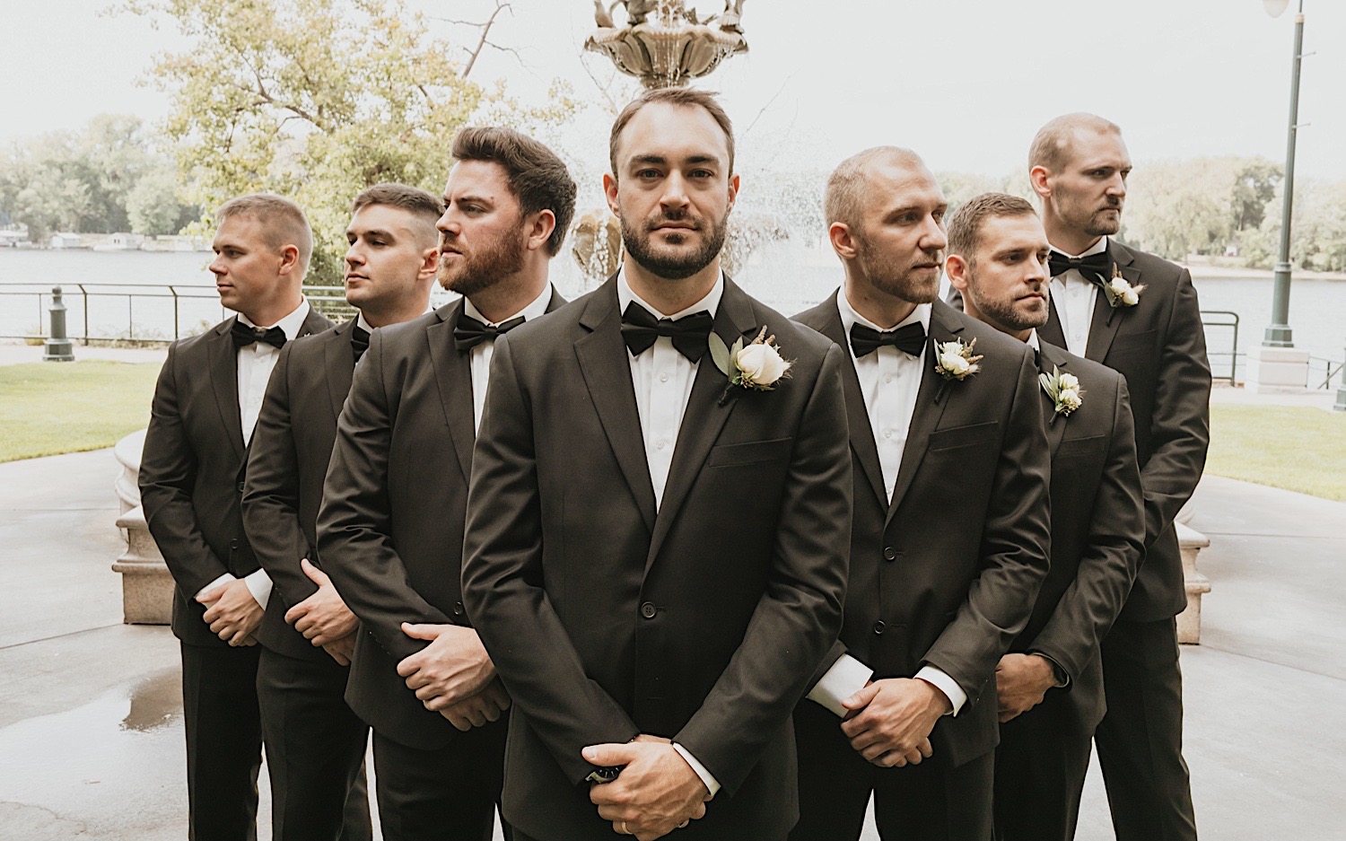 A groom looks at the camera with a serious face, on either side of him are his groomsmen looking off in the distance