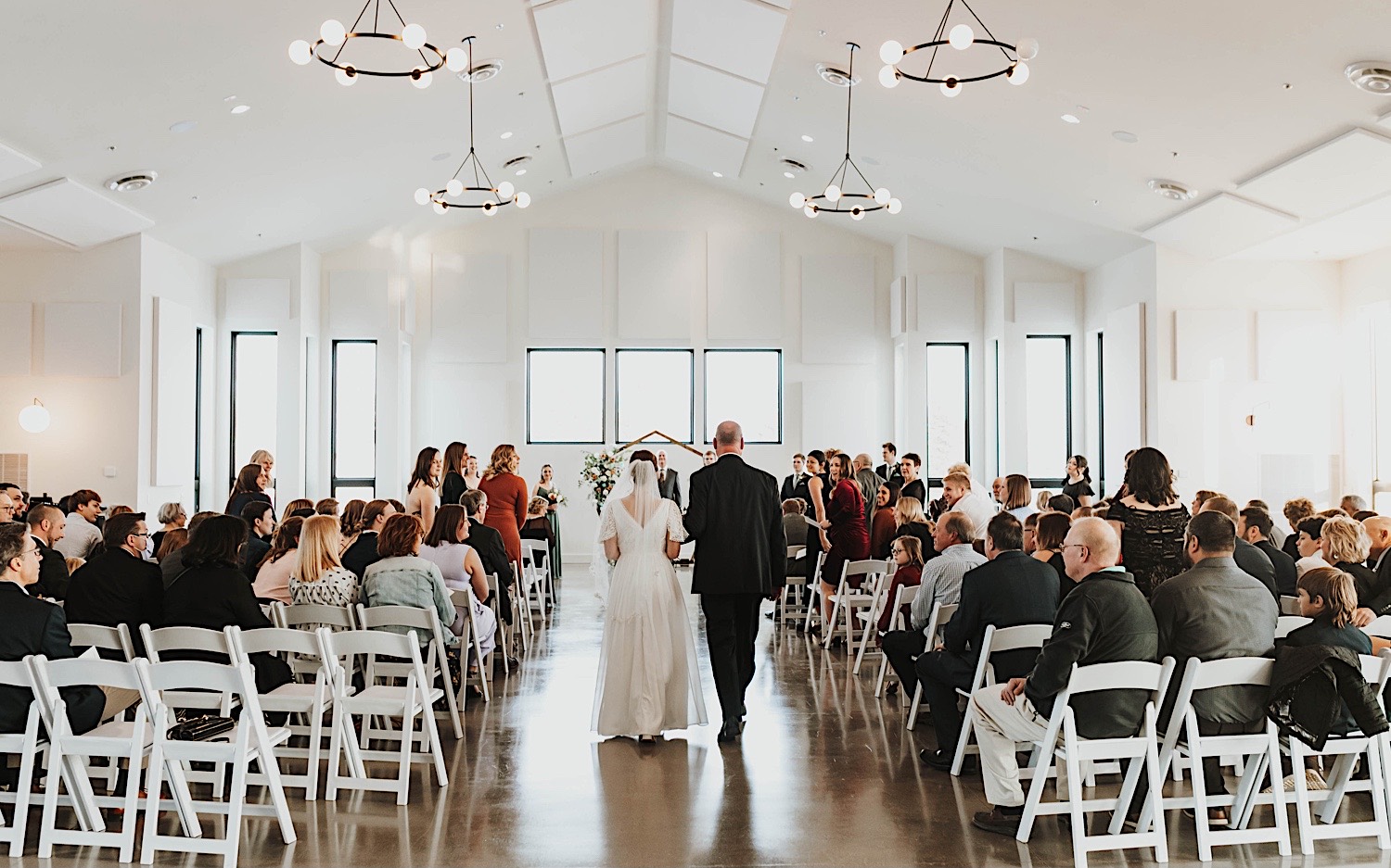 A bride walks down the aisle with her father during her wedding ceremony at her venue, Woodhaven Weddings + Events A bride walks down the aisle with her father during her wedding ceremony at her venue, Woodhaven Weddings + Events