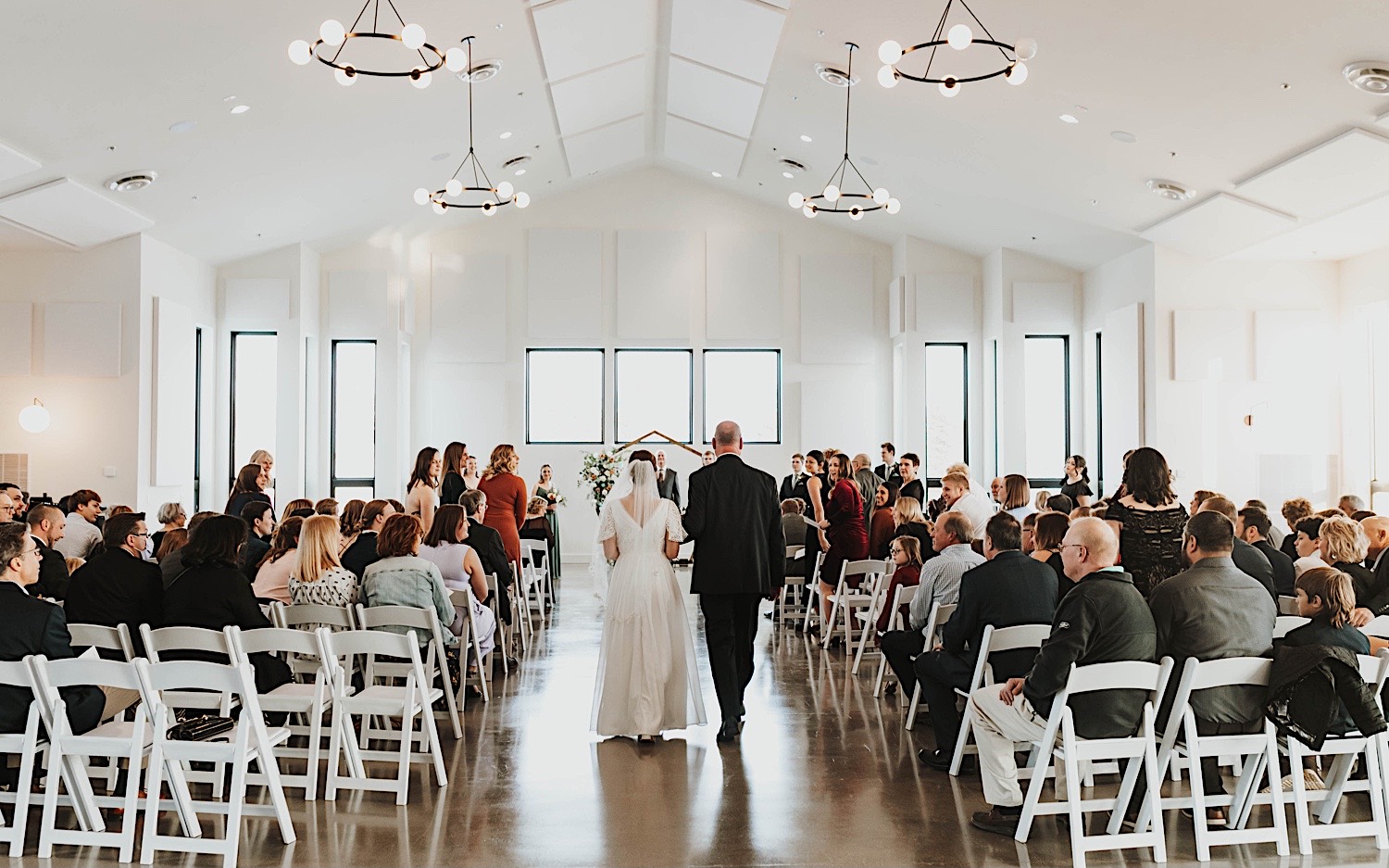 A bride walks down the aisle with her father during her wedding ceremony at her venue, Woodhaven Weddings + Events