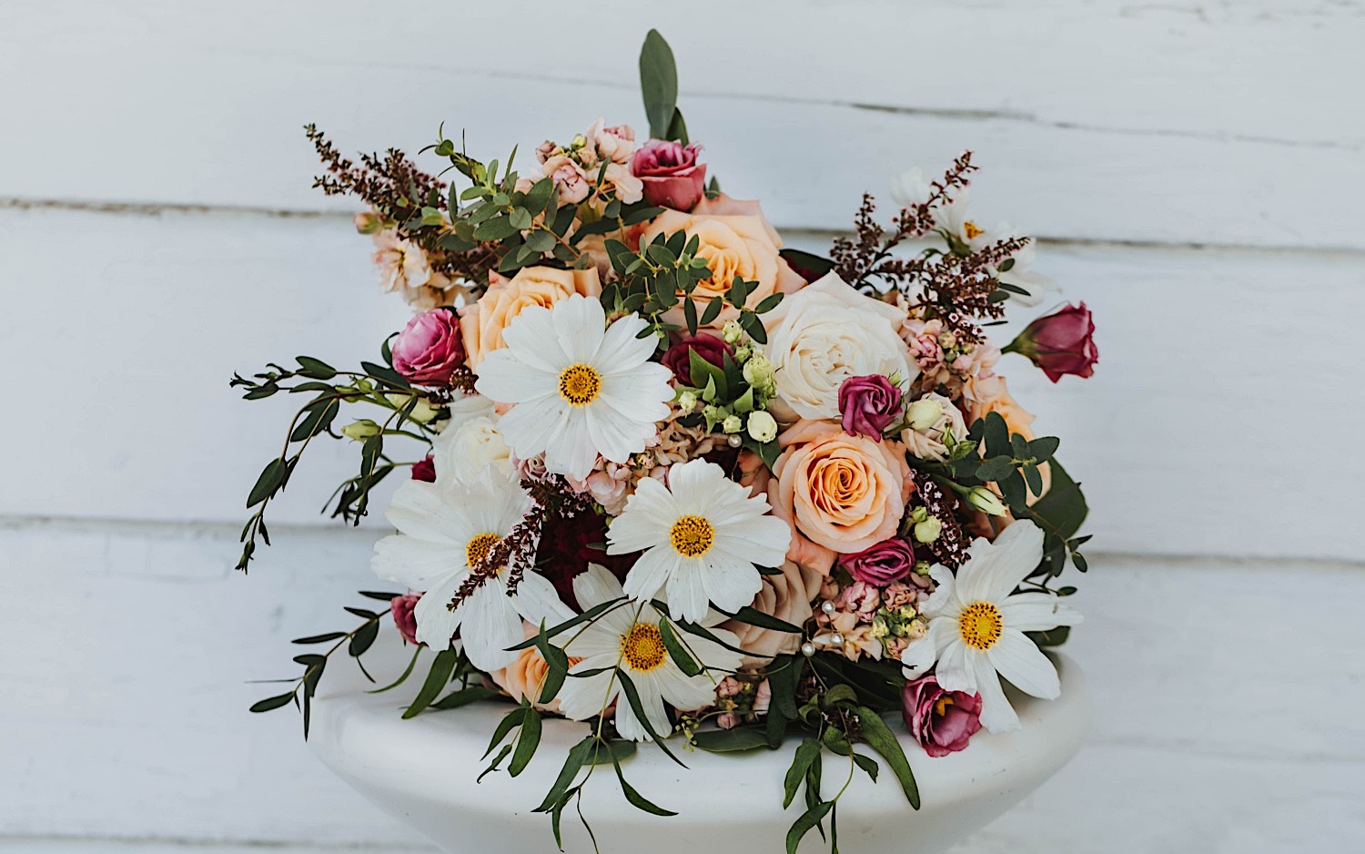 A flower bouquet rests on a small table outside of a white building A flower bouquet rests on a small table outside of a white building