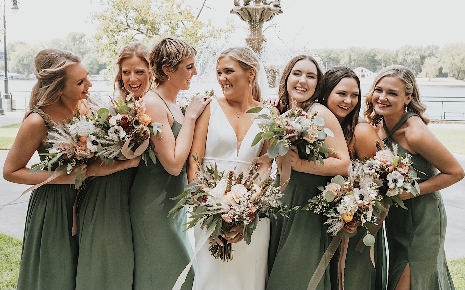 A bride smiles as her bridesmaids all surround her and smile