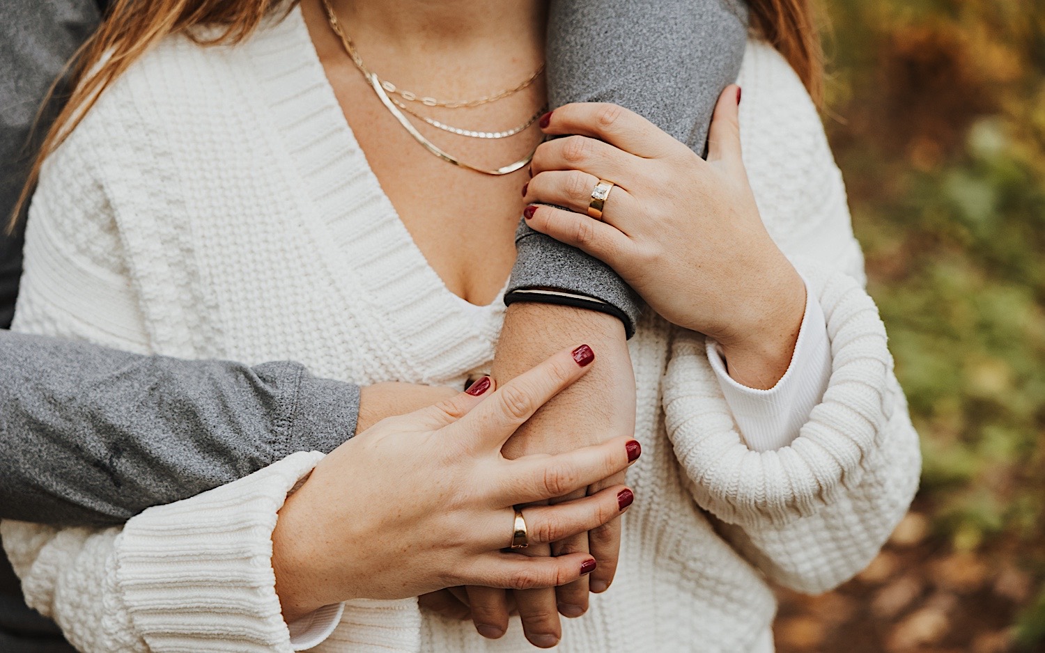 Close up photo of a woman's hand with an engagement ring on it as she's hugged from behind 