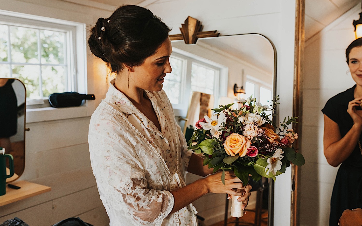 A woman smiles while holding a flower bouquet while standing inside of a getting ready space at the wedding venue Legacy Hill Farm