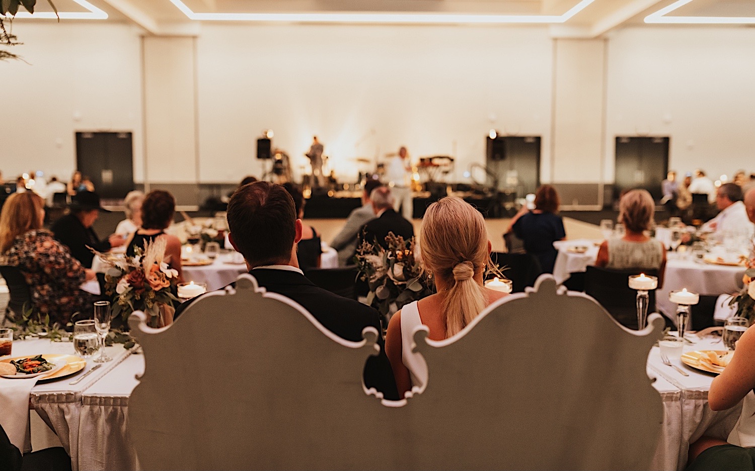 Photo of a bride and groom from behind with them seated looking out over their wedding reception at the La Crosse Center