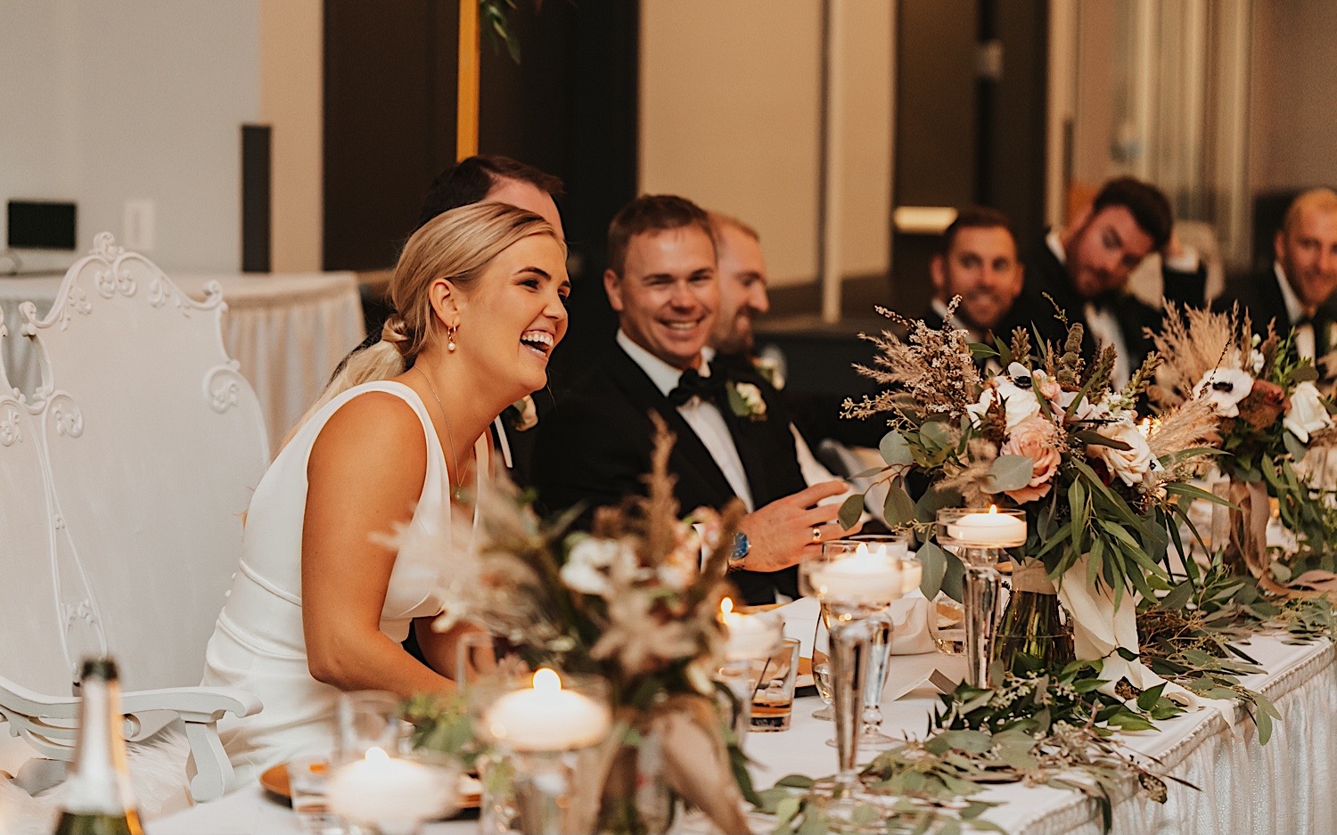 A bride laughs and smiles while seated during her wedding reception at The La Crosse Center