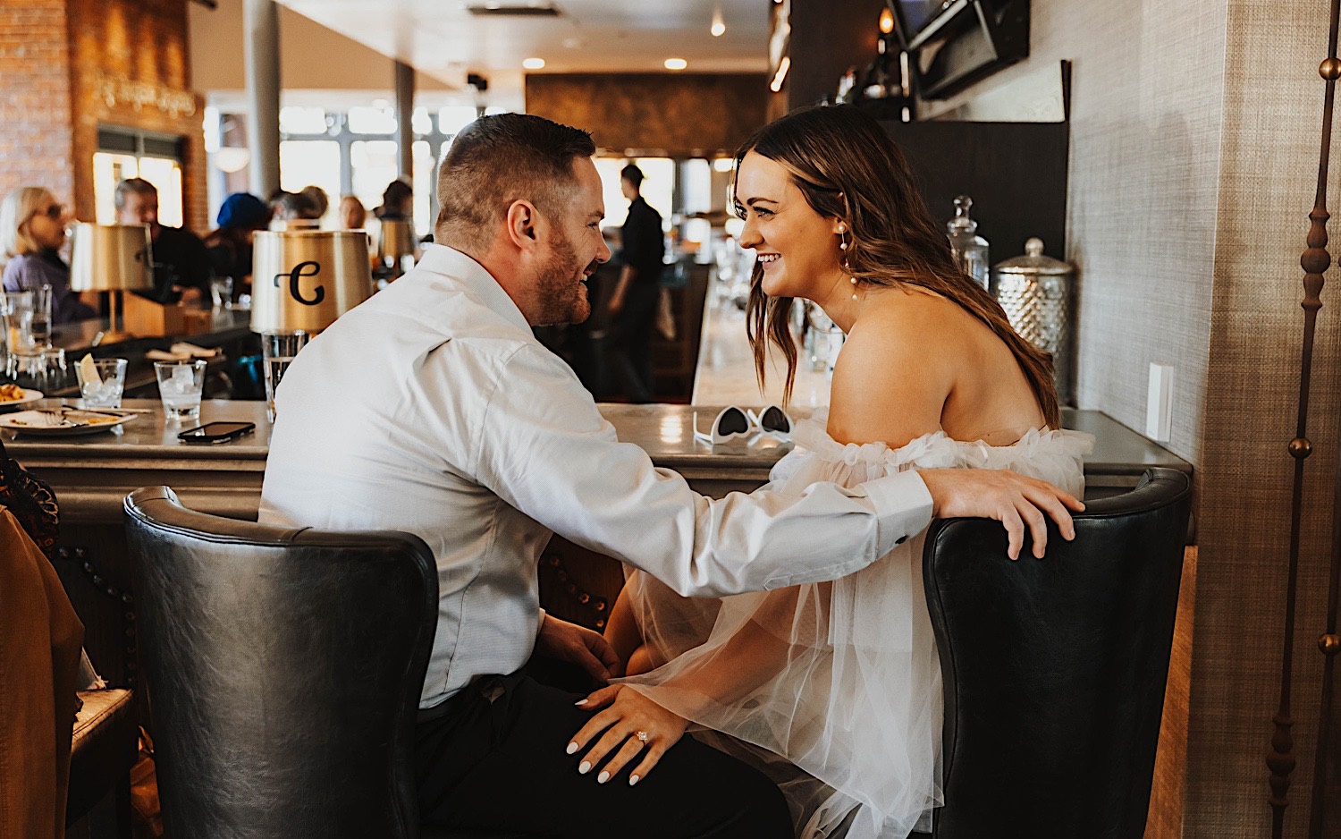 A couple sit together at a bar and smile at one another, photo taken by a Minneapolis wedding photographer