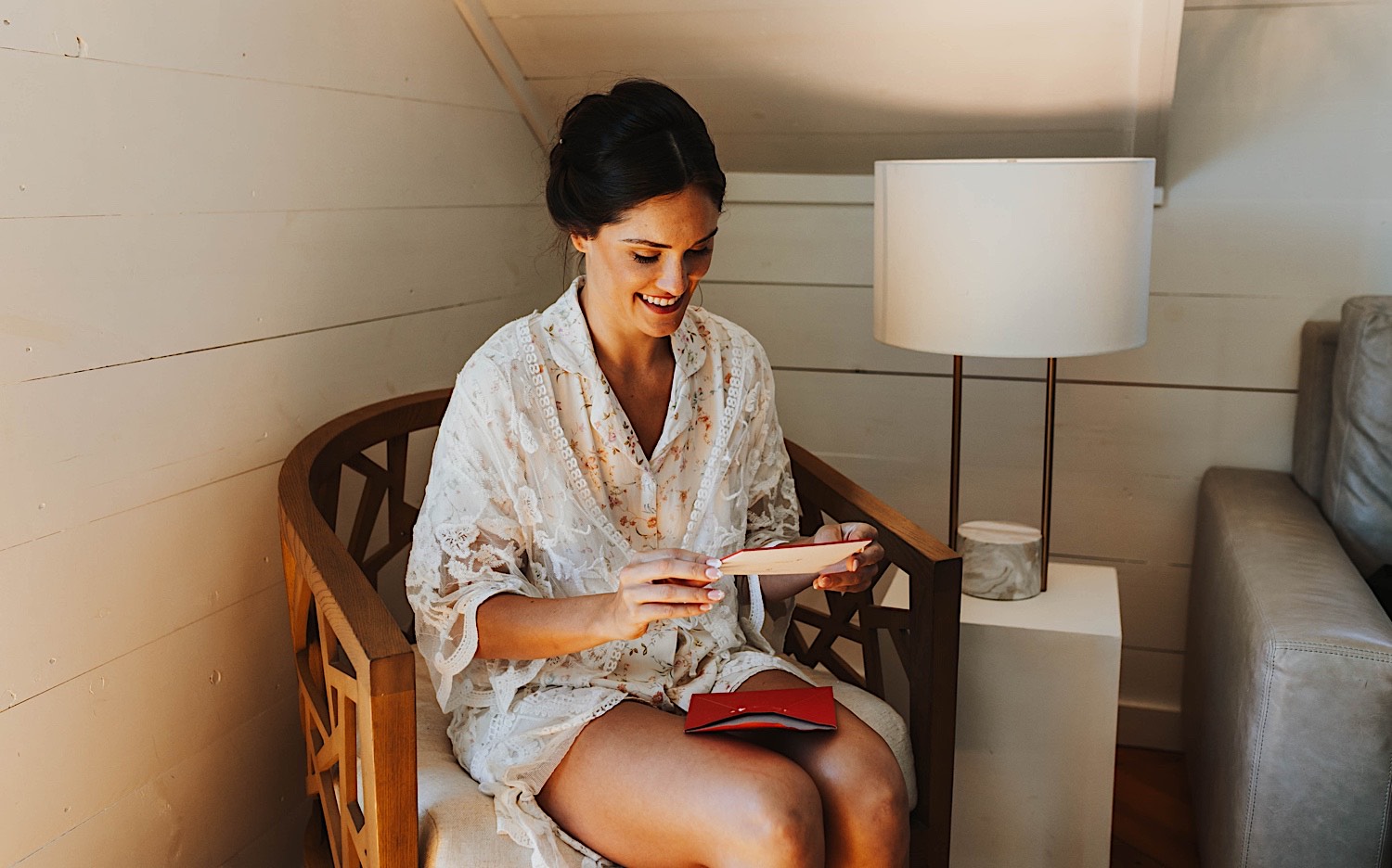 A woman sits in a chair and reads a card on the morning of her wedding while inside the getting ready space at Legacy Hill Farm