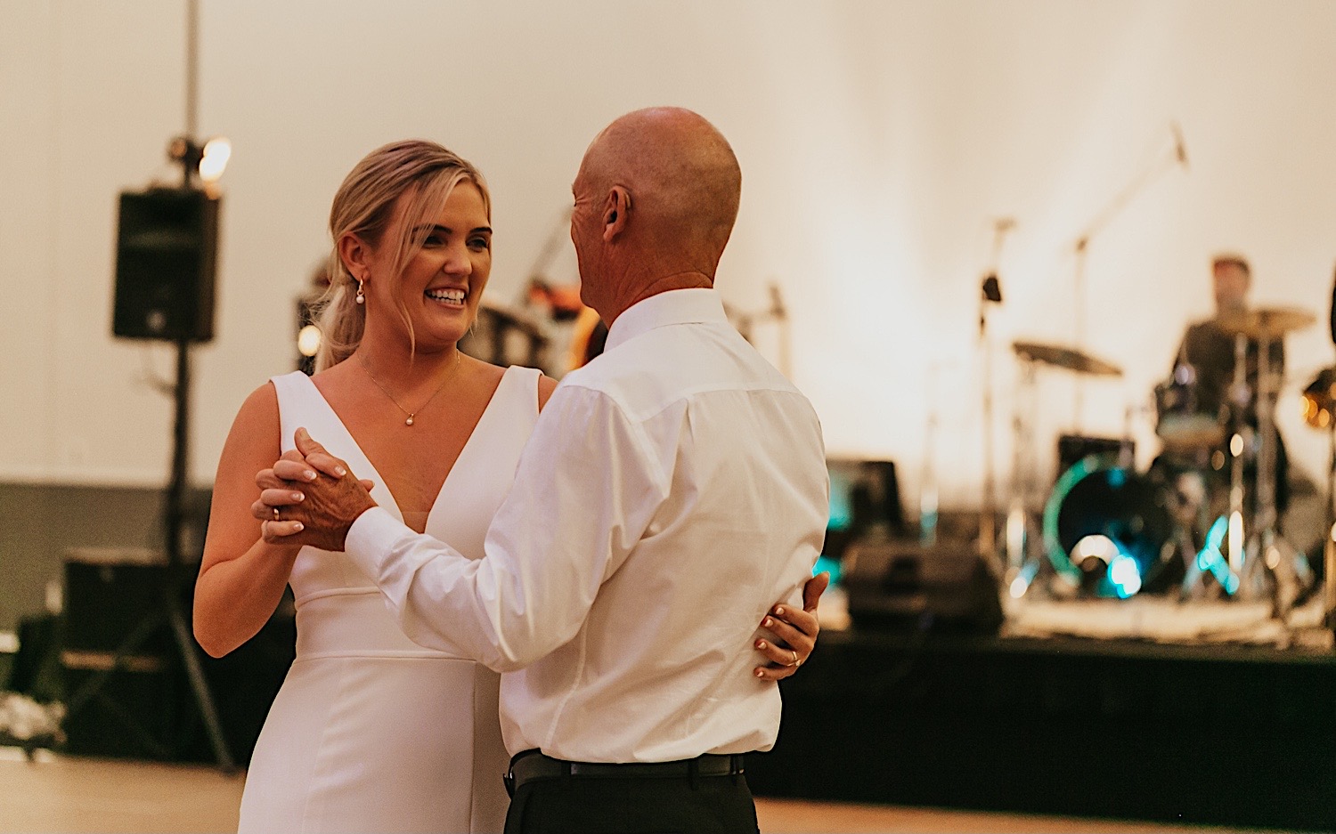 A bride smiles as she dances with her father during her wedding reception at the La Crosse Center while the live band plays behind them