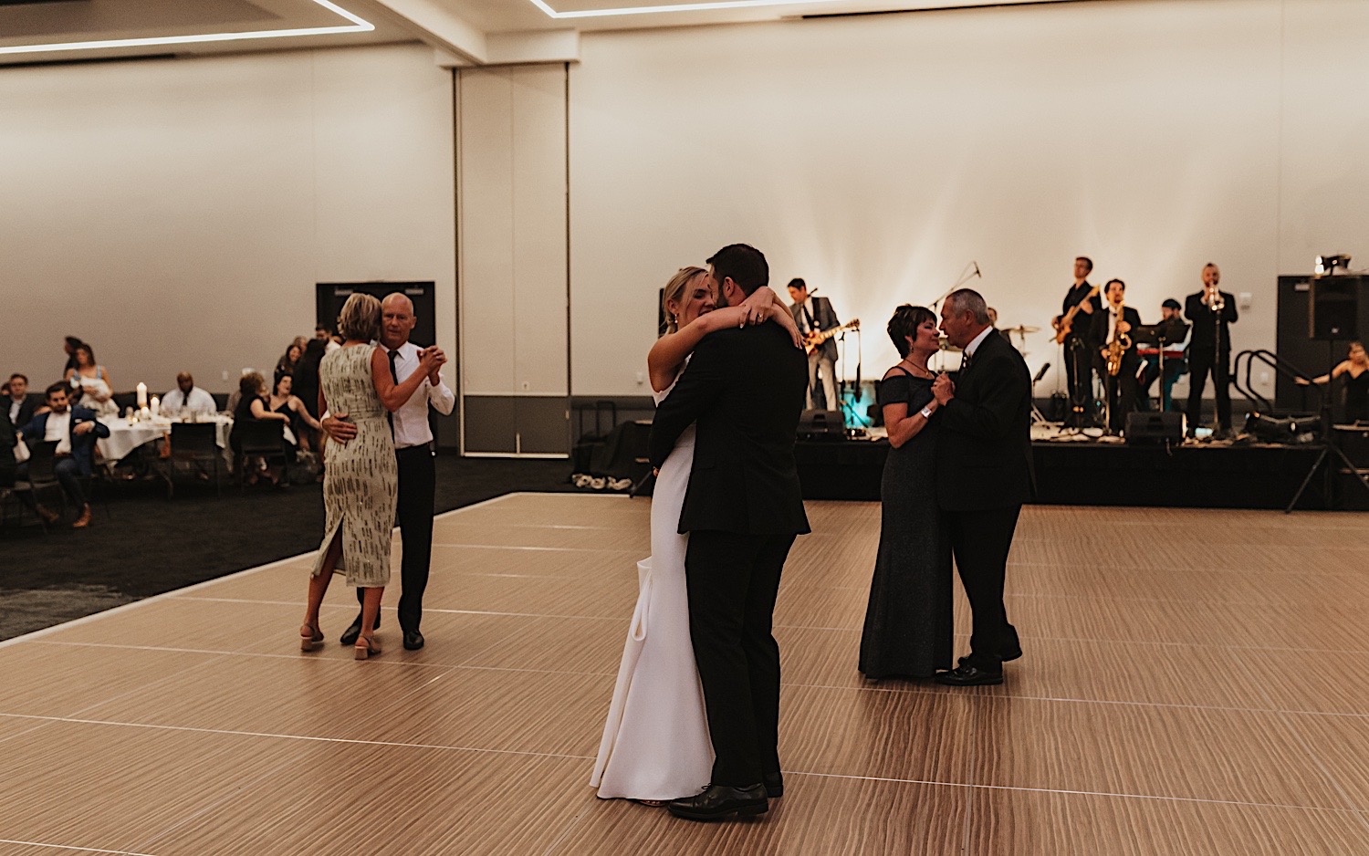 A bride and groom dance together with their parents dancing together on either side of  them during their wedding reception at the La Crosse Center
