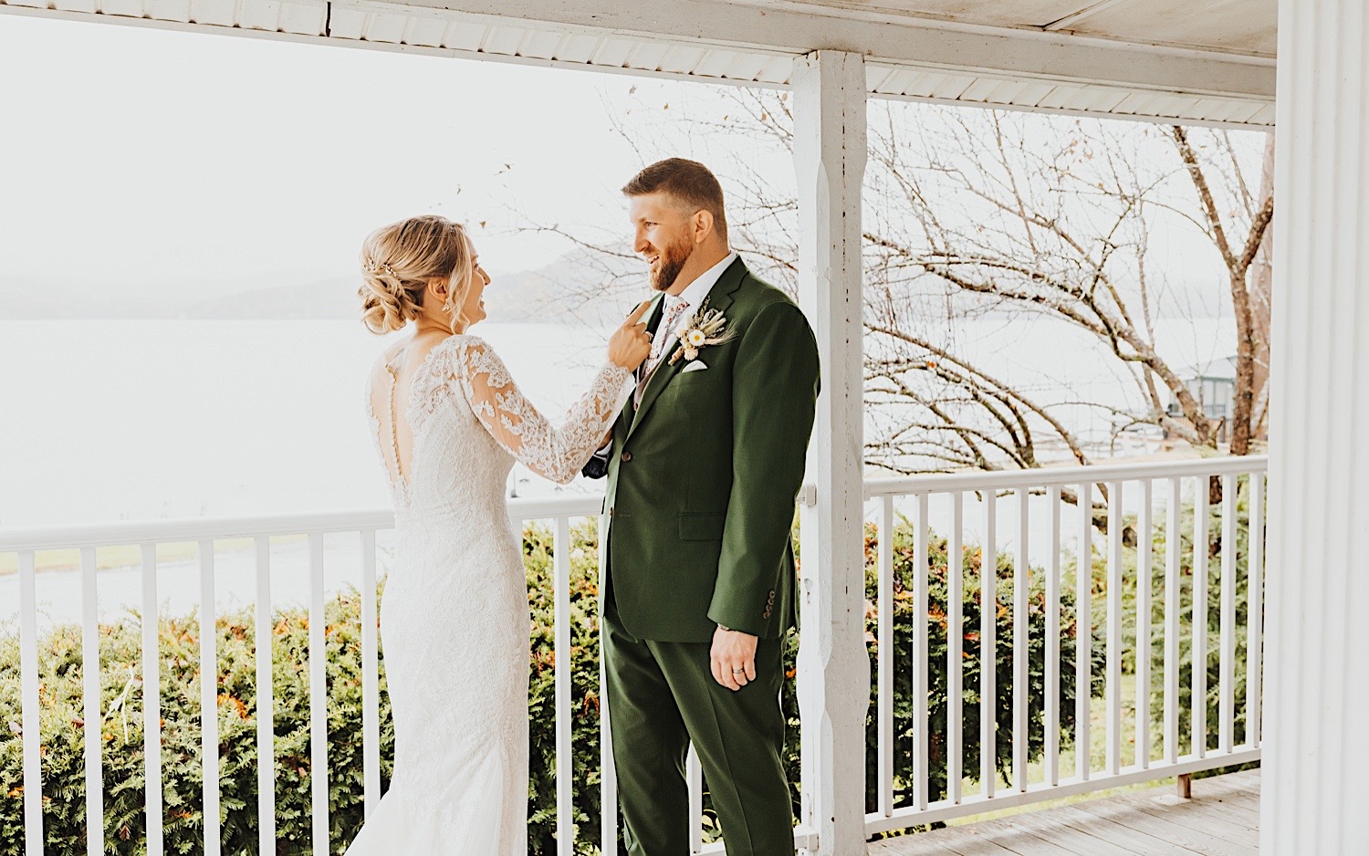 At bride and groom smile at one another while standing on the front porch of a house at Lake Bomoseen
