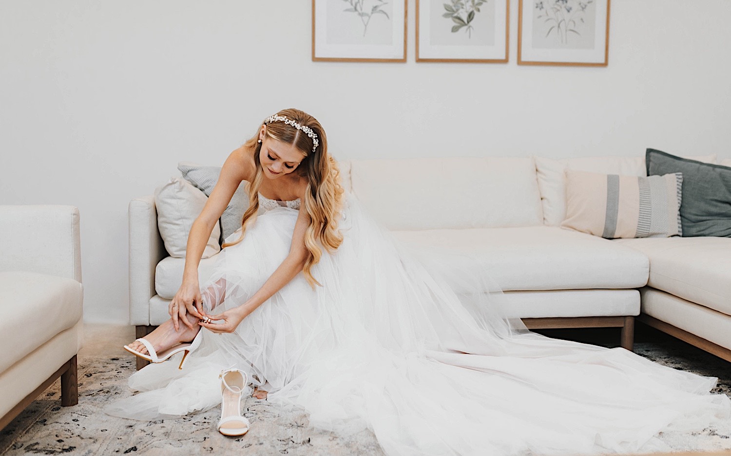 A bride sits on a couch and puts on her shoes while getting ready for her wedding day at The Aisling