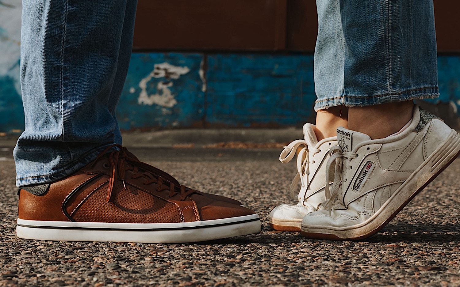 Close up photo of a man and woman's legs and shoes, the woman is on her tip toes in order to kiss the man