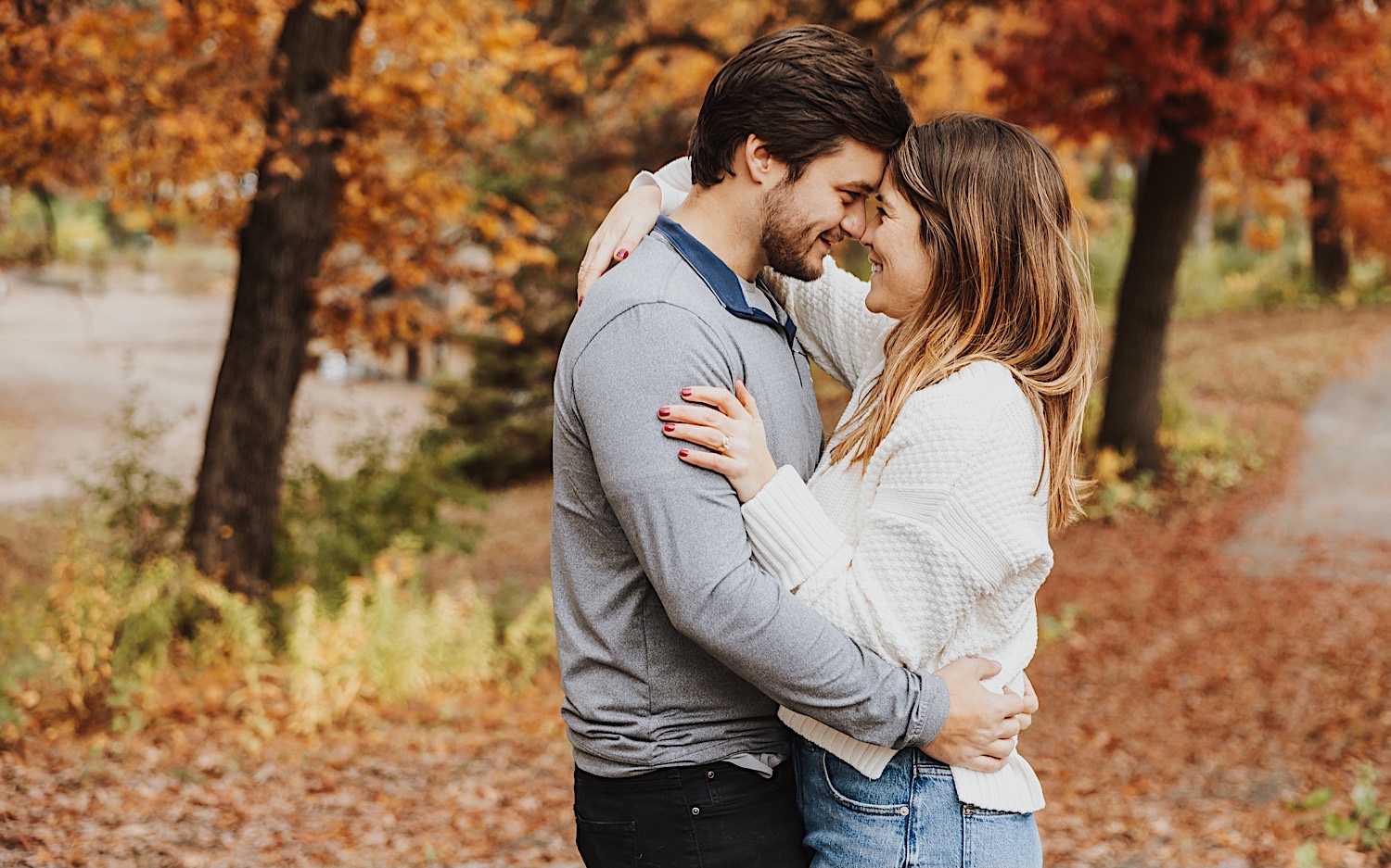 A couple embrace and smile at one another during their engagement session in Theodore Wirth Park of Minneapolis