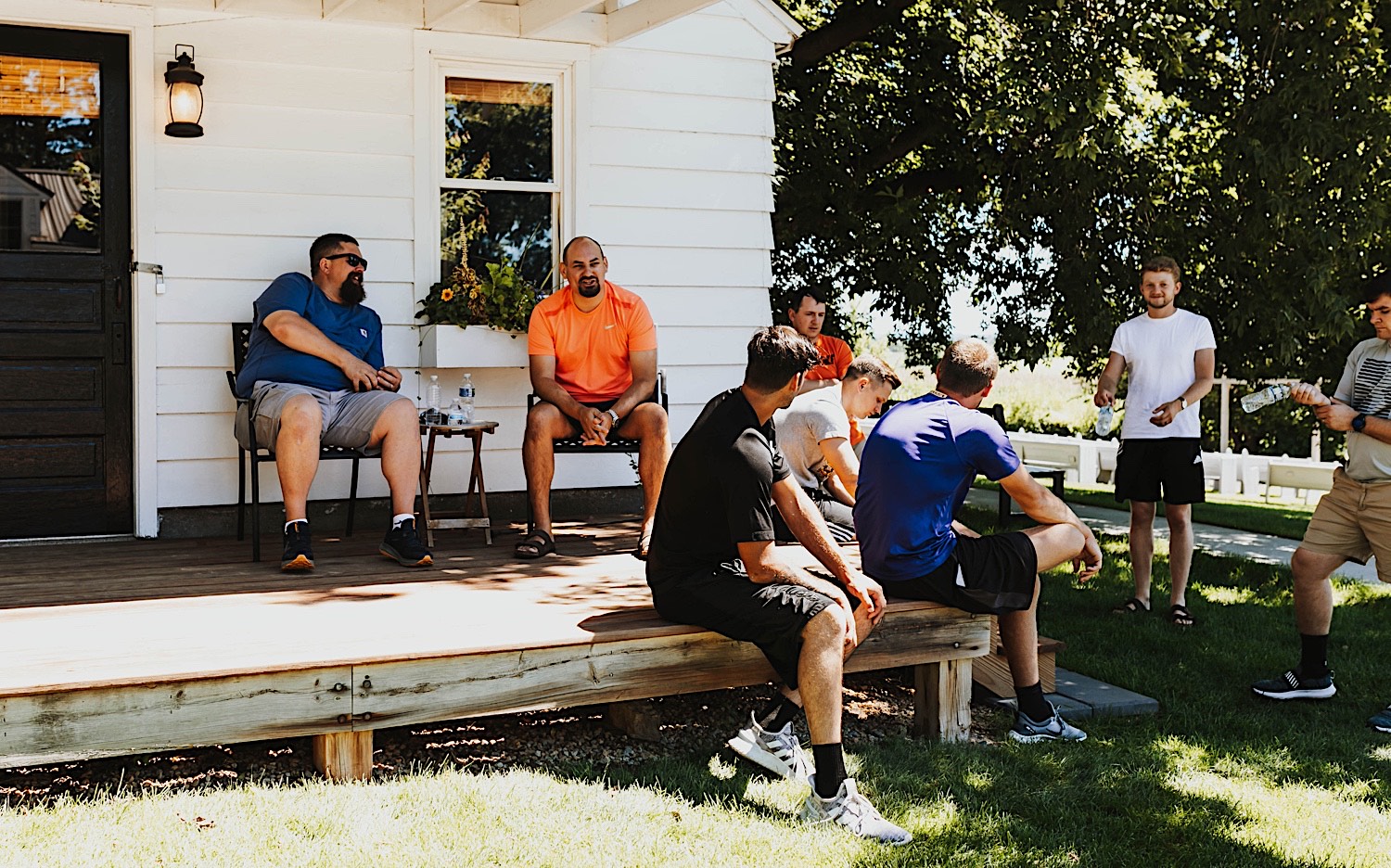 A group of men sit and stand in a circle outside of a white building on the grounds of Legacy Hill Farm before getting ready for the wedding that will be taking place there
