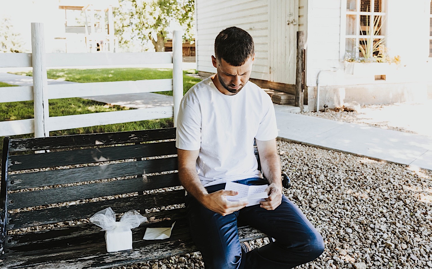 A man sits on a bench and reads a card attached to a gift he received on the morning of his wedding day at Legacy Hill Farm