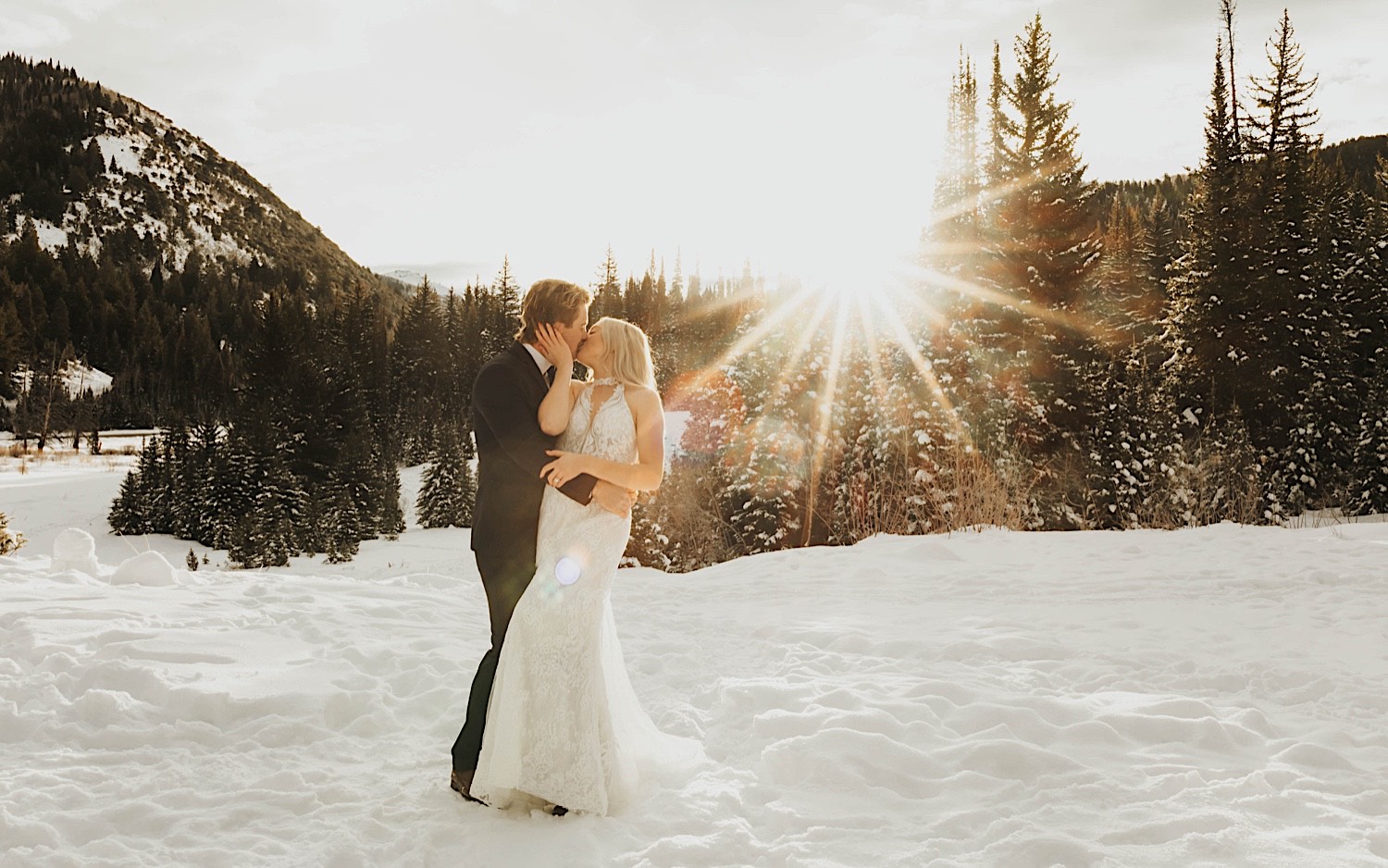 As the sun sets behind them on a snow covered forest near Salt Lake City, a bride and groom kiss one another standing in the snow after their elopement As the sun sets behind them on a snow covered forest near Salt Lake City, a bride and groom kiss one another standing in the snow after their elopement